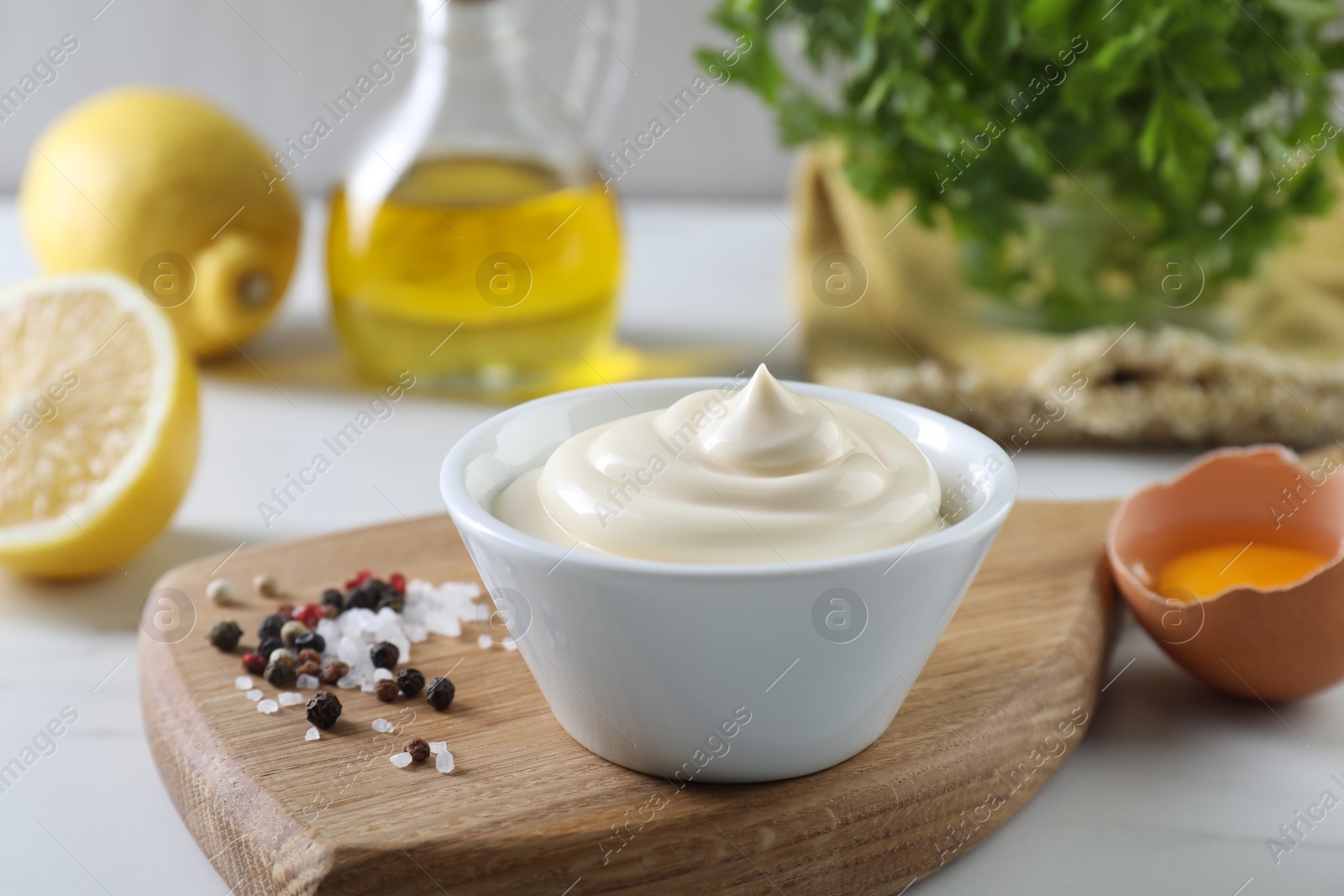 Photo of Tasty mayonnaise sauce in bowl, ingredients and spices on white table, closeup