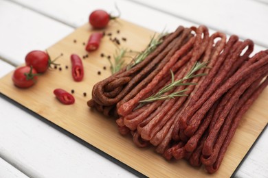 Photo of Delicious kabanosy with rosemary, peppercorn, chilli and tomatoes on white wooden table, closeup