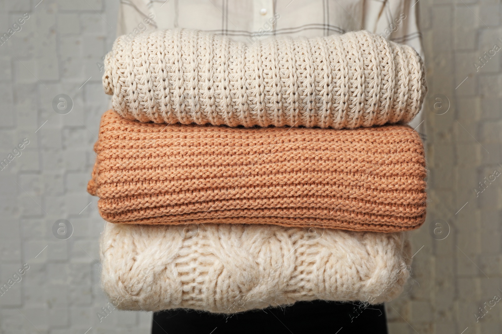 Photo of Woman holding stack of folded warm knitted sweaters, closeup