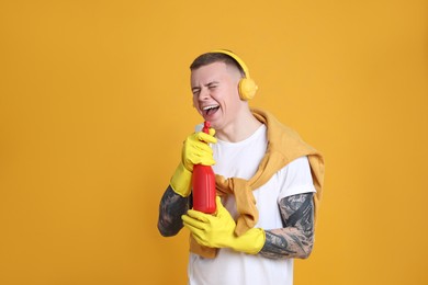 Photo of Handsome young man with bottle of detergent singing on orange background. Space for text
