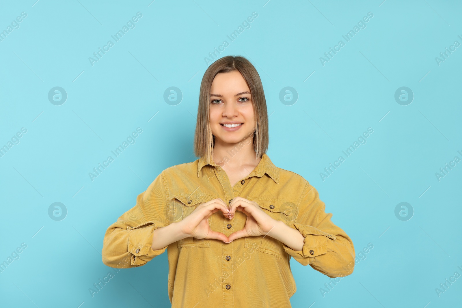 Photo of Young woman making heart with hands on turquoise background. Volunteer concept