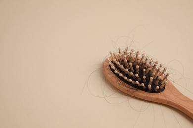 Photo of Wooden brush with lost hair on beige background, closeup. Space for text