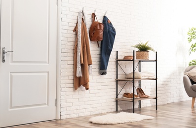 Stylish hallway interior with door, comfortable furniture and clothes on brick wall