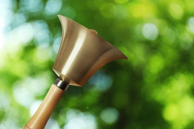 Shiny school bell with wooden handle outdoors. Bokeh effect