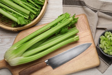 Photo of Fresh ripe celery and knife on white wooden table, flat lay