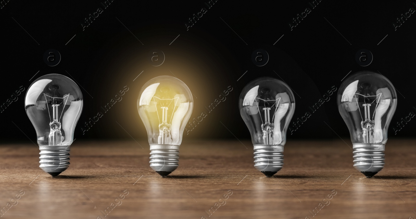 Image of Idea concept. Glowing light bulb among others on wooden table against black background, banner design 