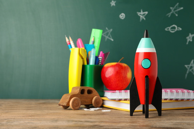 Photo of Bright toy rocket and school supplies on wooden desk. Space for text