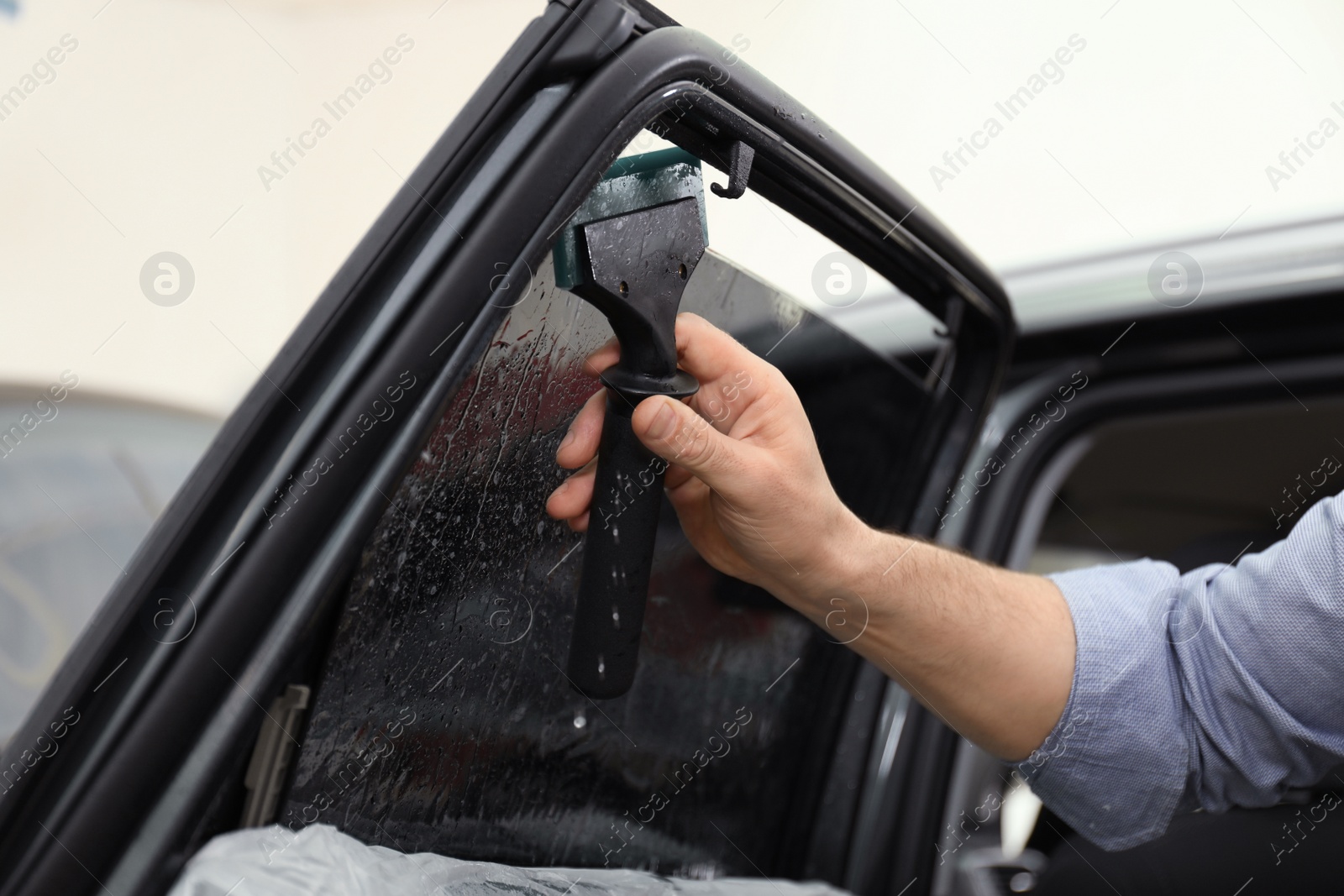 Photo of Worker washing tinted car window in workshop, closeup
