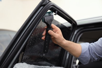Worker washing tinted car window in workshop, closeup