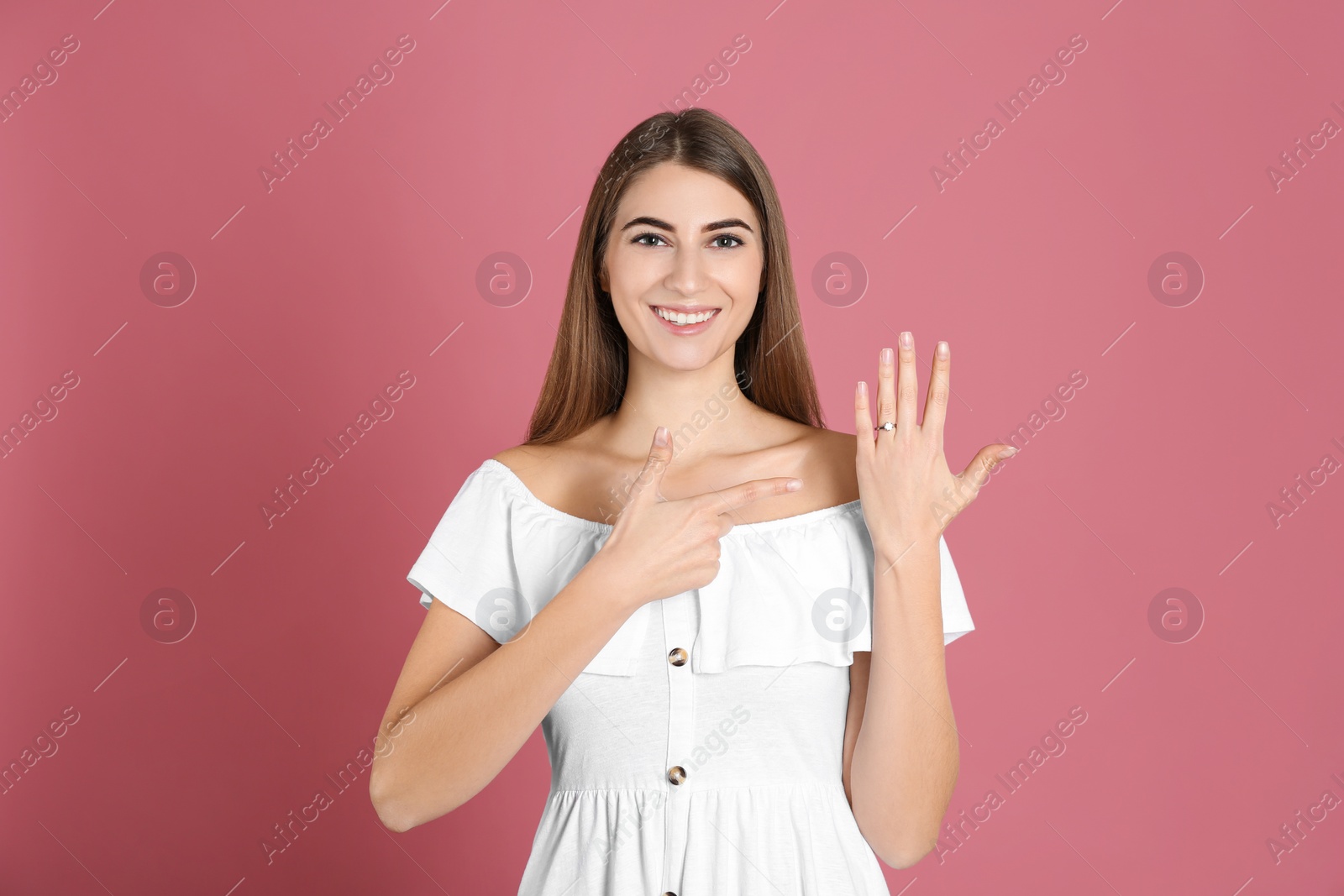 Photo of Happy young woman wearing beautiful engagement ring on pink background