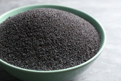 Photo of Poppy seeds in bowl on grey table, closeup