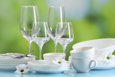 Photo of Set of many clean dishware, cutlery, flowers and glasses on light blue table against blurred green background