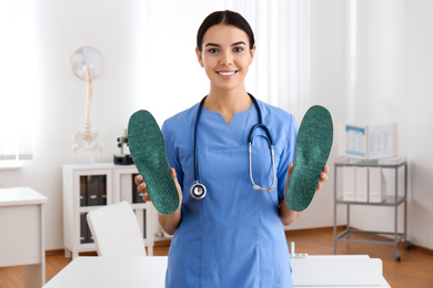 Photo of Young female orthopedist showing insoles in clinic