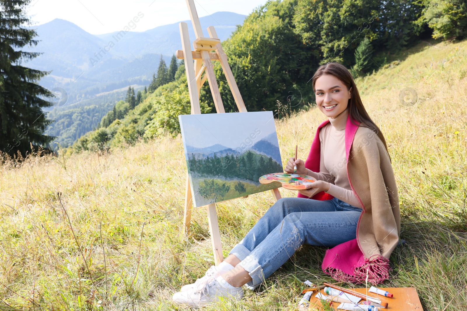 Photo of Young woman drawing on easel in mountains