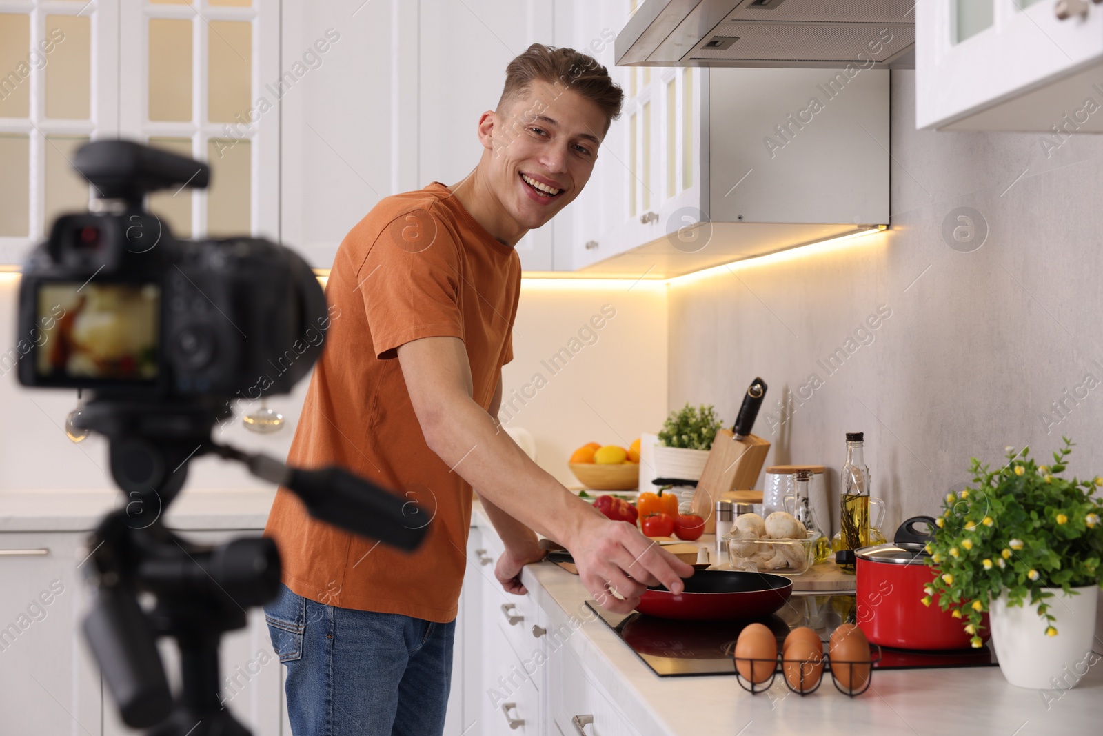 Photo of Smiling food blogger cooking while recording video in kitchen