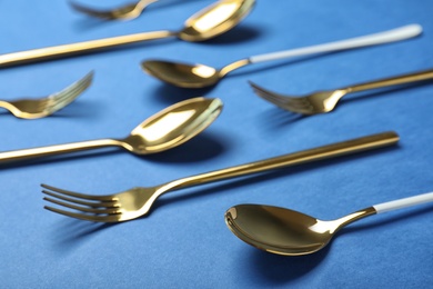 Set of new gold cutlery on blue background, closeup