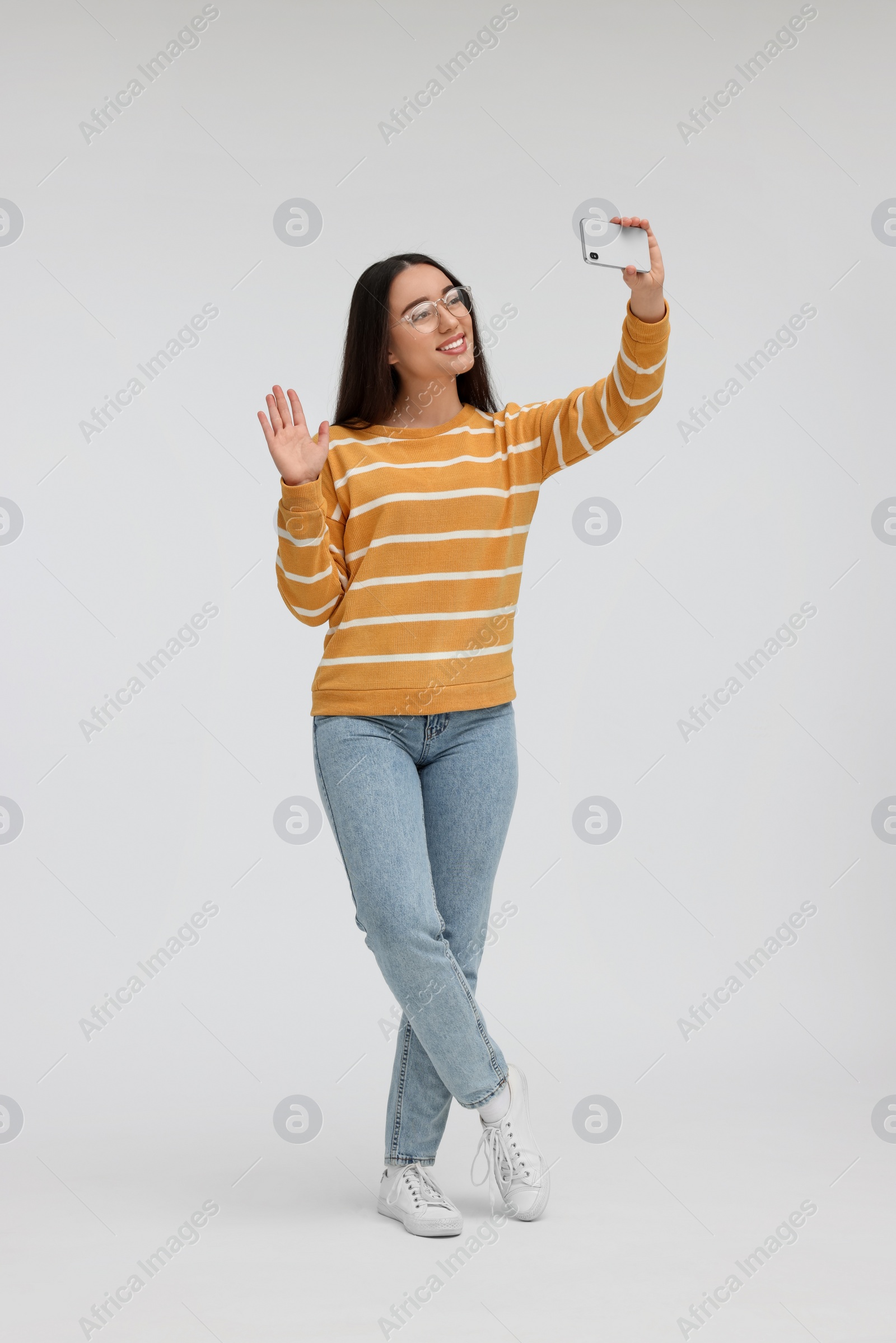 Photo of Smiling young woman taking selfie with smartphone on white background