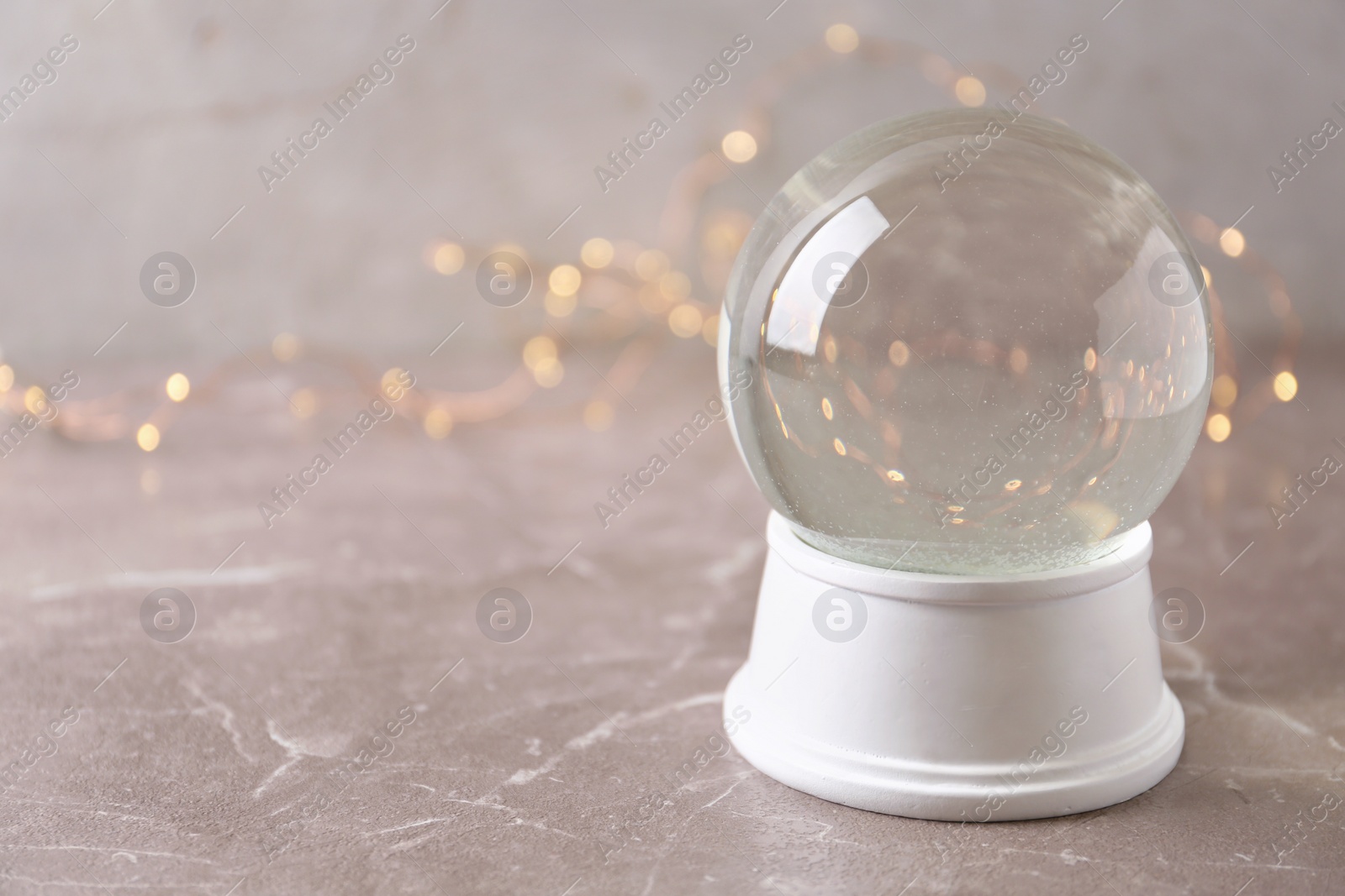 Photo of Snow globe on marble table against festive lights, space for text. Christmas season