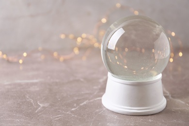 Photo of Snow globe on marble table against festive lights, space for text. Christmas season