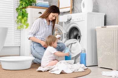 Mother with her daughter washing baby clothes in bathroom