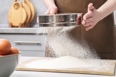Photo of Woman sieving flour at table in kitchen, closeup