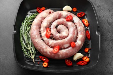 Photo of Pan with raw homemade sausage, chili pepper, garlic and rosemary on grey table, above view