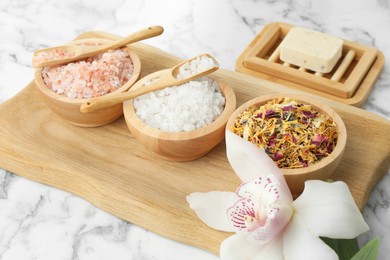 Spa composition with sea salt, dry flowers, soap bar and orchid on white marble table