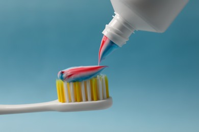 Photo of Squeezing toothpaste onto brush against light blue background, closeup