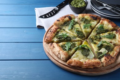 Photo of Delicious pizza with pesto, cheese and arugula on blue wooden table. Space for text