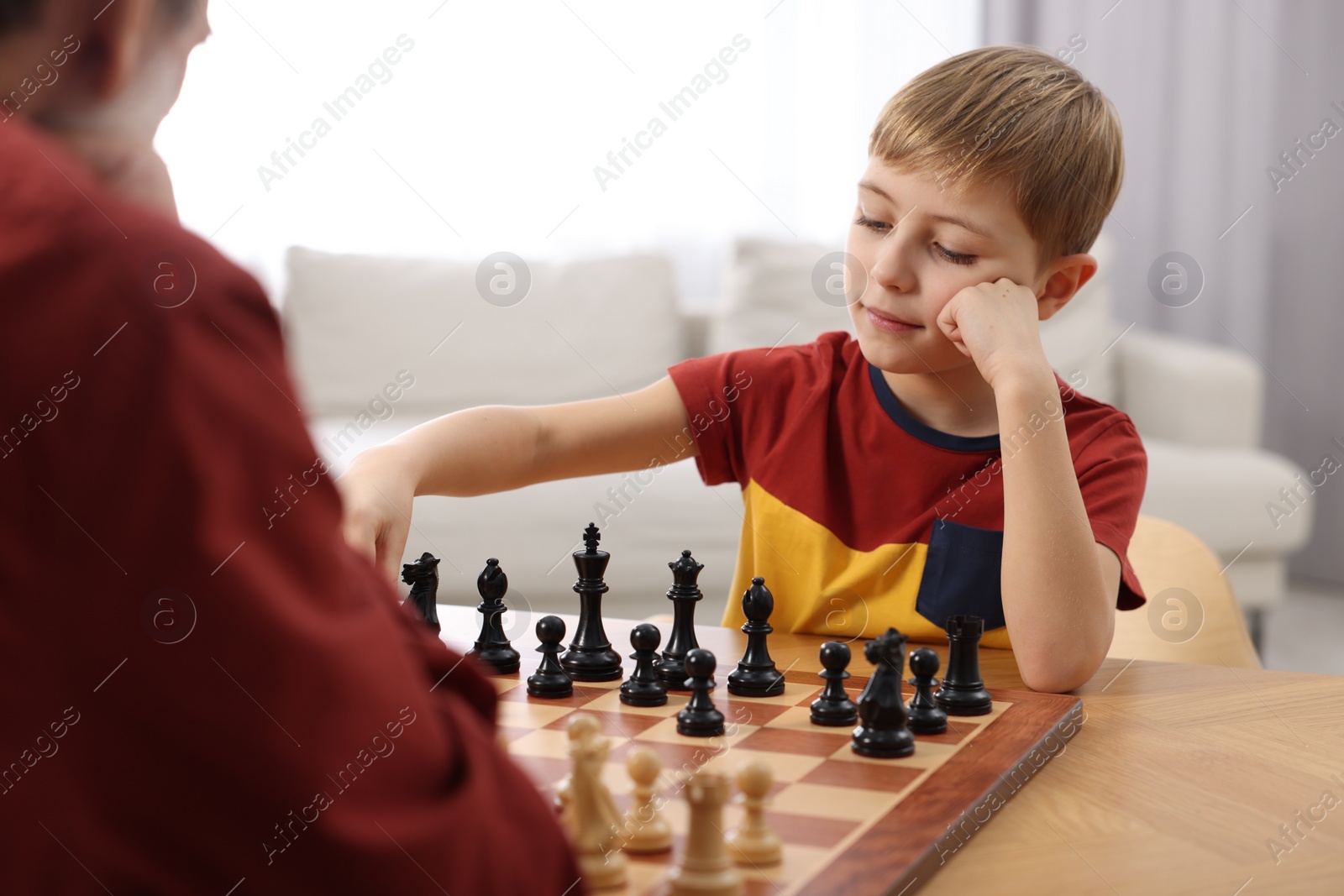 Photo of Little boy playing chess with his grandfather at table in room