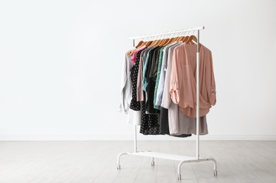 Wardrobe rack with stylish clothes near white wall indoors. Space for text