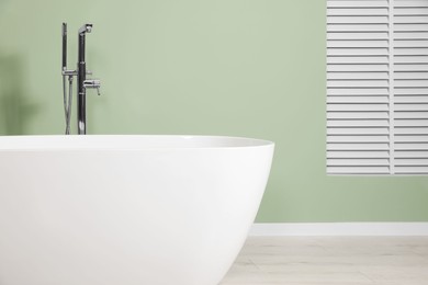 Photo of Modern ceramic tub near light green wall in bathroom. Interior design