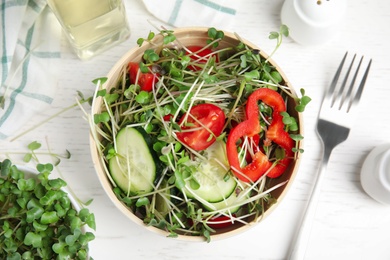 Salad with fresh organic microgreen in bowl on white table, flat lay