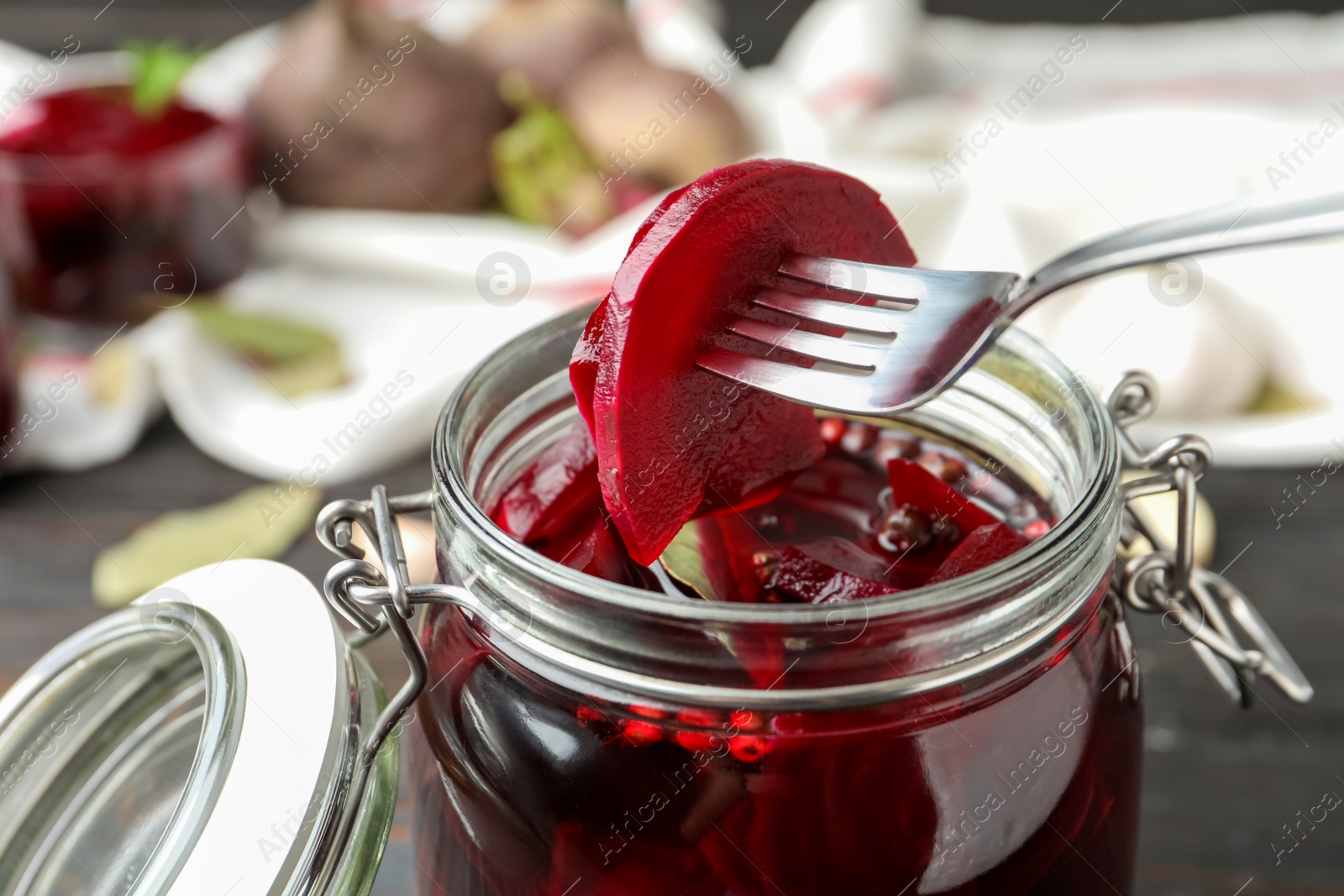 Photo of Fork with pickled beets over glass jar on wooden table, closeup