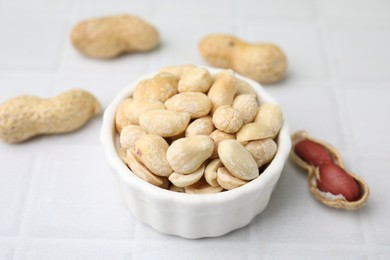 Photo of Fresh peeled peanuts in bowl on white tiled table, closeup