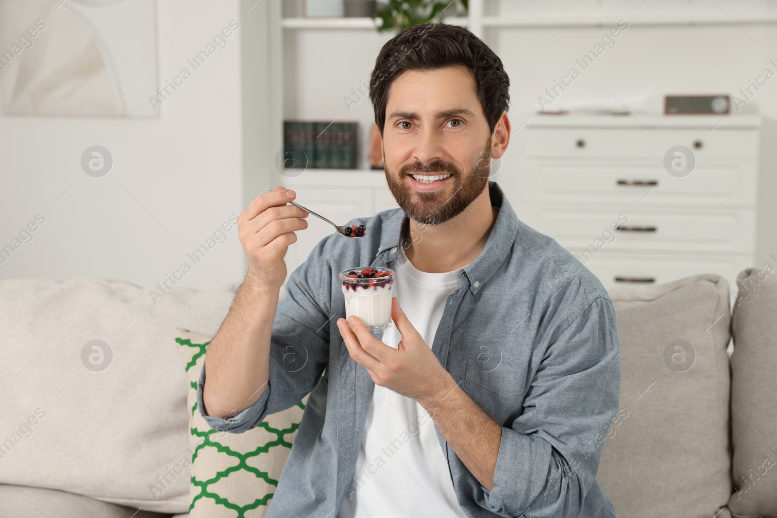 Photo of Handsome man with delicious yogurt on sofa at home