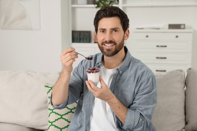 Photo of Handsome man with delicious yogurt on sofa at home
