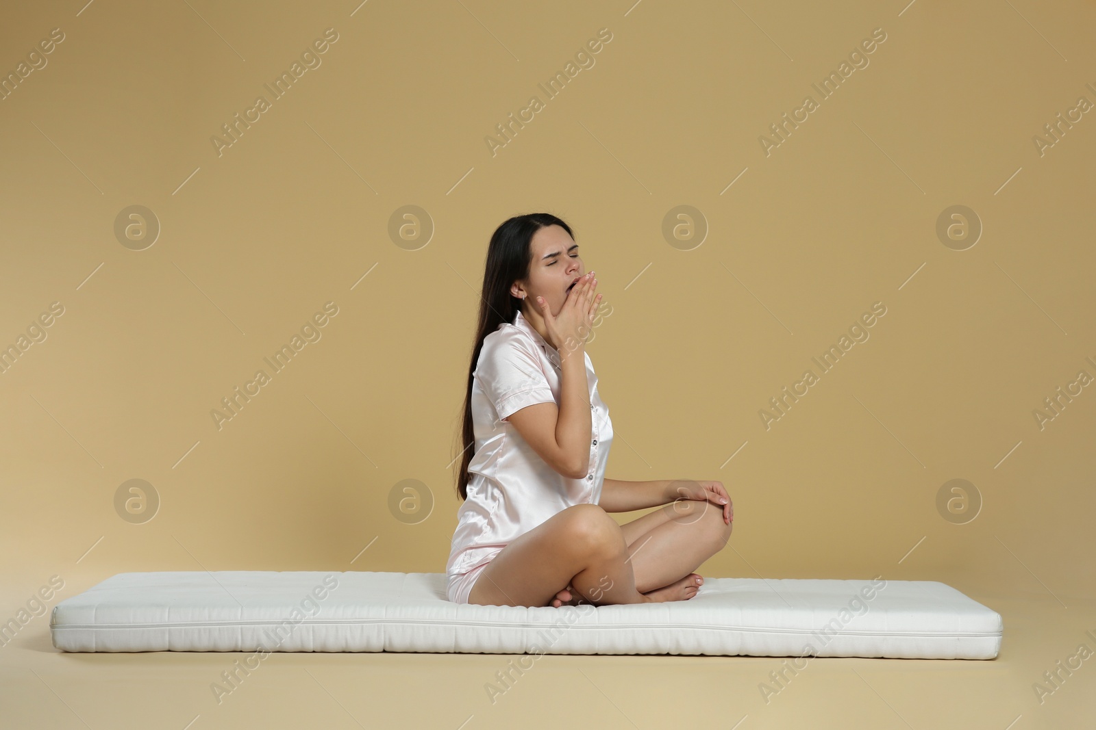 Photo of Young woman yawning on soft mattress against beige background