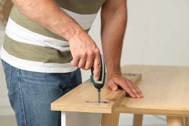Man with electric screwdriver assembling furniture at table indoors, closeup
