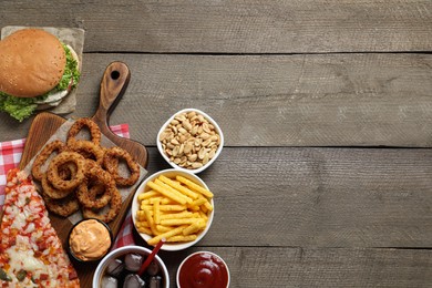 French fries, onion rings and other fast food on wooden table, flat lay with space for text