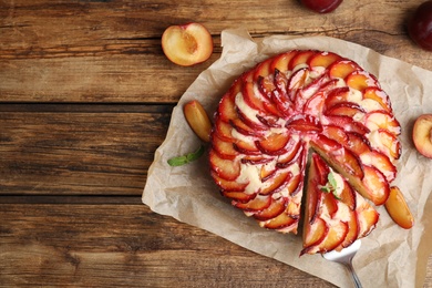 Delicious cake with plums on wooden table, flat lay