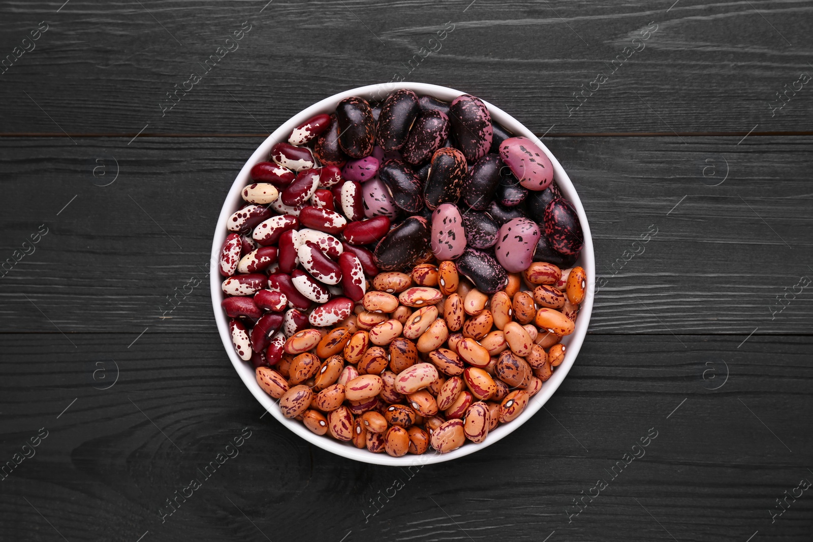 Photo of Different kinds of dry kidney beans in bowl on wooden table, top view