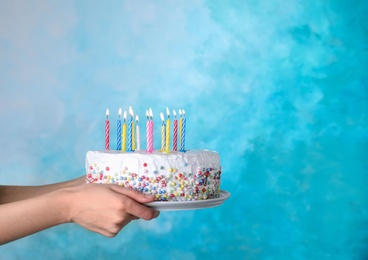 Photo of Woman holding birthday cake with burning candles on light blue background, closeup. Space for text