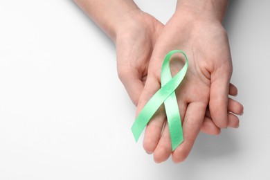 Photo of World Mental Health Day. Woman holding green ribbon on white background, top view with space for text