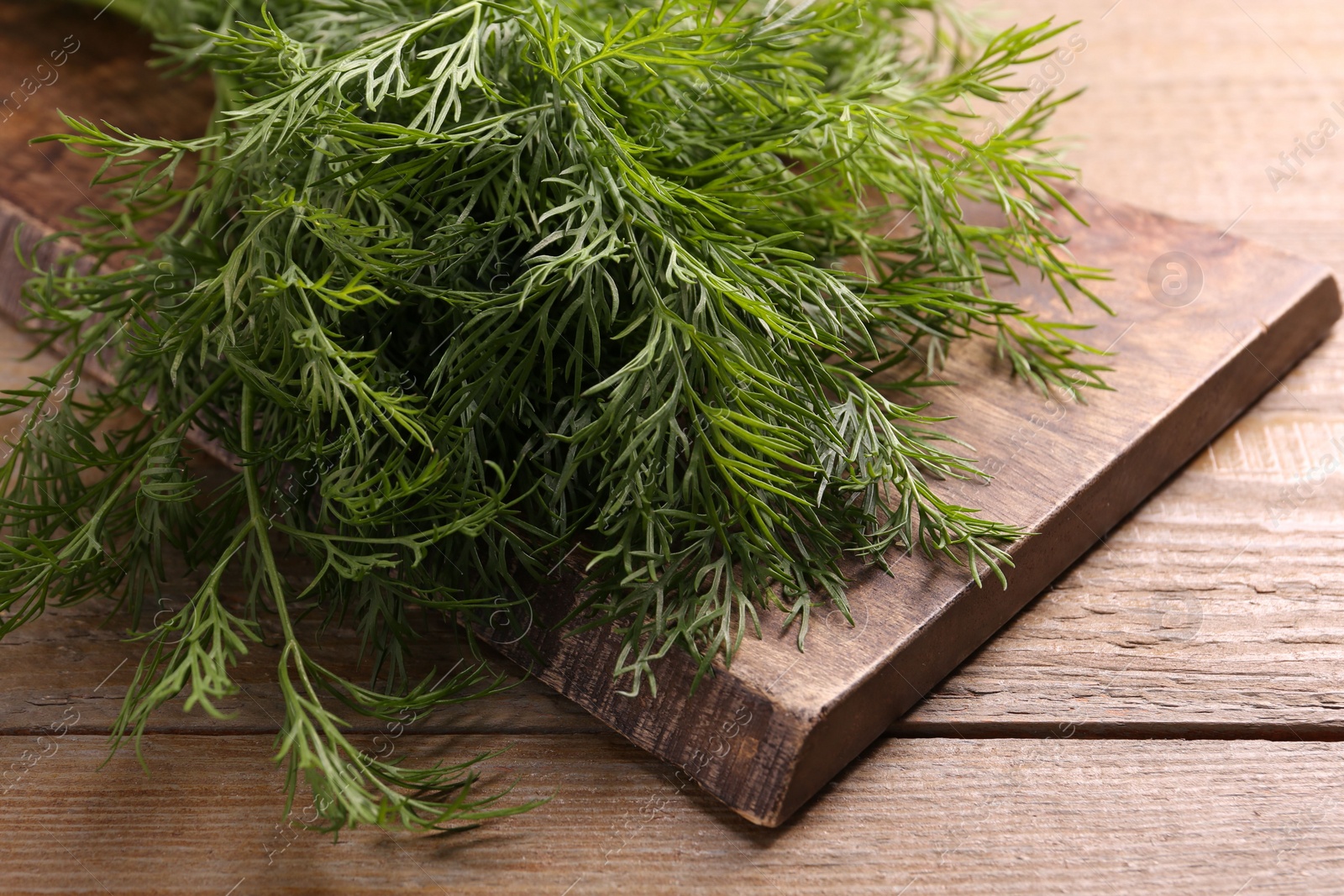 Photo of Board with sprigs of fresh dill on wooden table, closeup