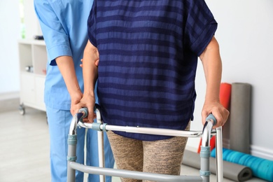 Photo of Caretaker helping elderly woman with walking frame indoors, closeup
