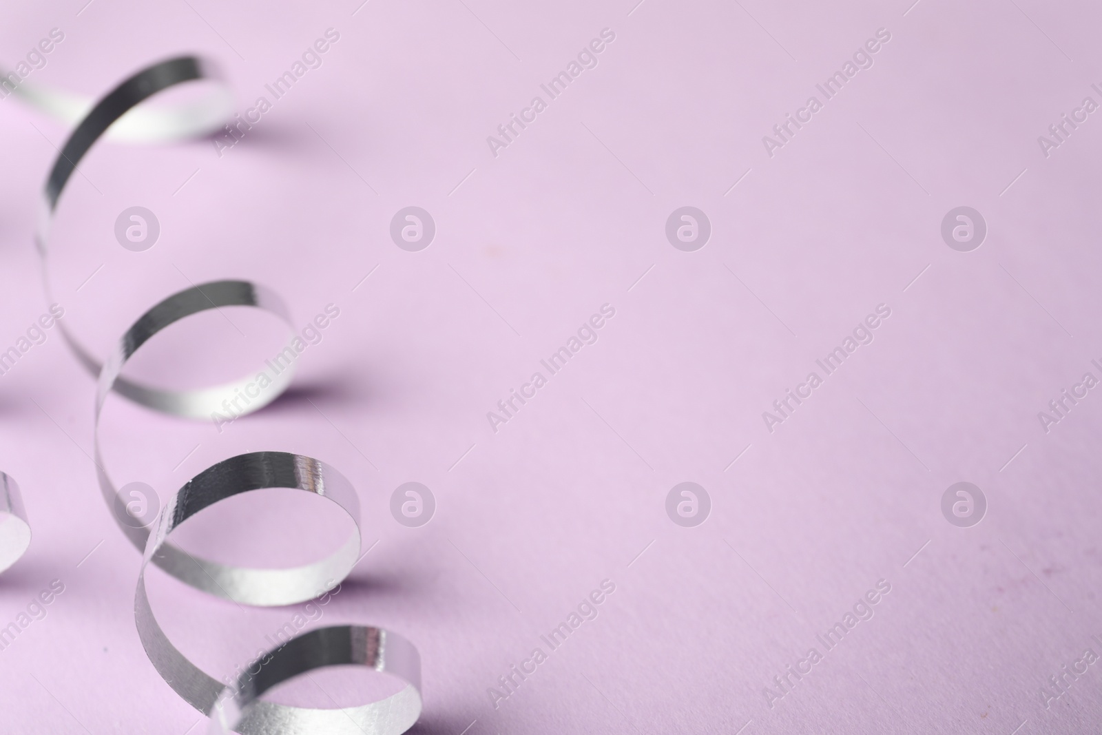 Photo of Shiny serpentine streamer on lilac background, closeup. Space for text