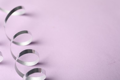 Shiny serpentine streamer on lilac background, closeup. Space for text