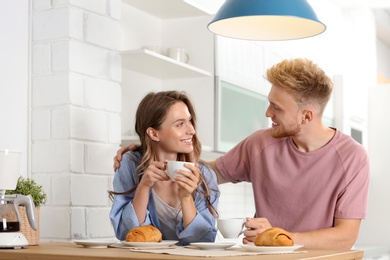 Happy young couple having breakfast at table in kitchen