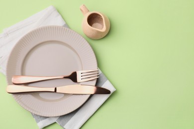 Photo of Clean plate with cutlery, saucepan and napkin on light green background, flat lay. Space for text